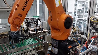 Industrial KUKA robot collecting injectors and feeding them to a vision system where they are inspected and verified.